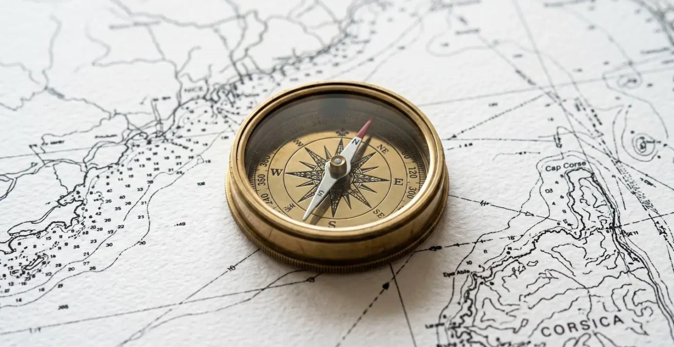 Gros plan sur une carte maritime de la Méditerranée montrant la zone entre Nice et la Corse avec un compas de navigation posé sur une table moderne